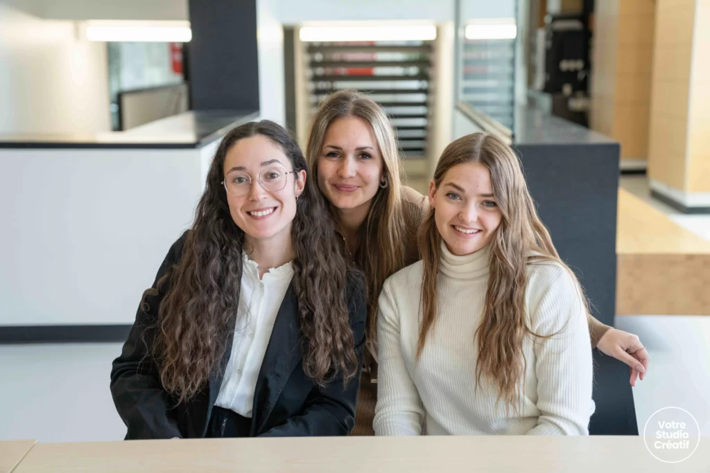 Trois étudiantes participant à une épreuve académique souriant à la caméra